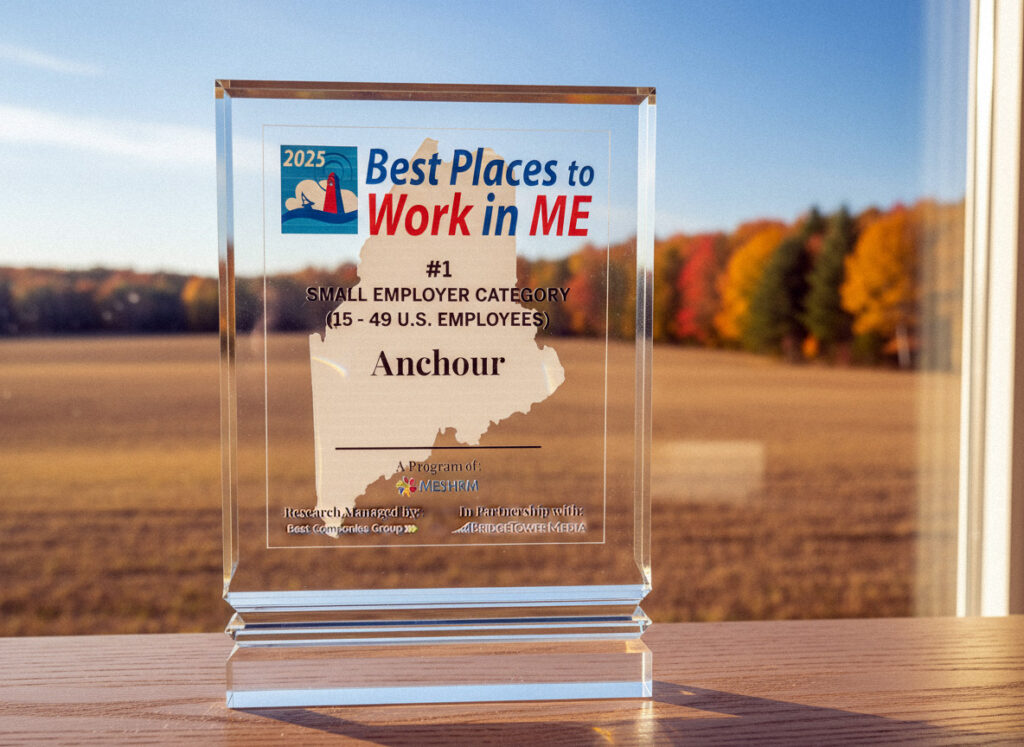 A glass award reads Best Places to Work in ME 2025, #1 Small Employer Category (15-49 U.S. Employees), Anchour, set on a windowsill with autumn trees in the background.