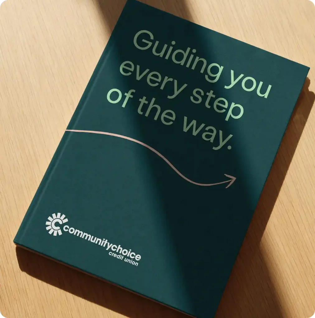 A dark green folder on a wooden surface reads Guiding you every step of the way. with the Community Choice Credit Union logo at the bottom.