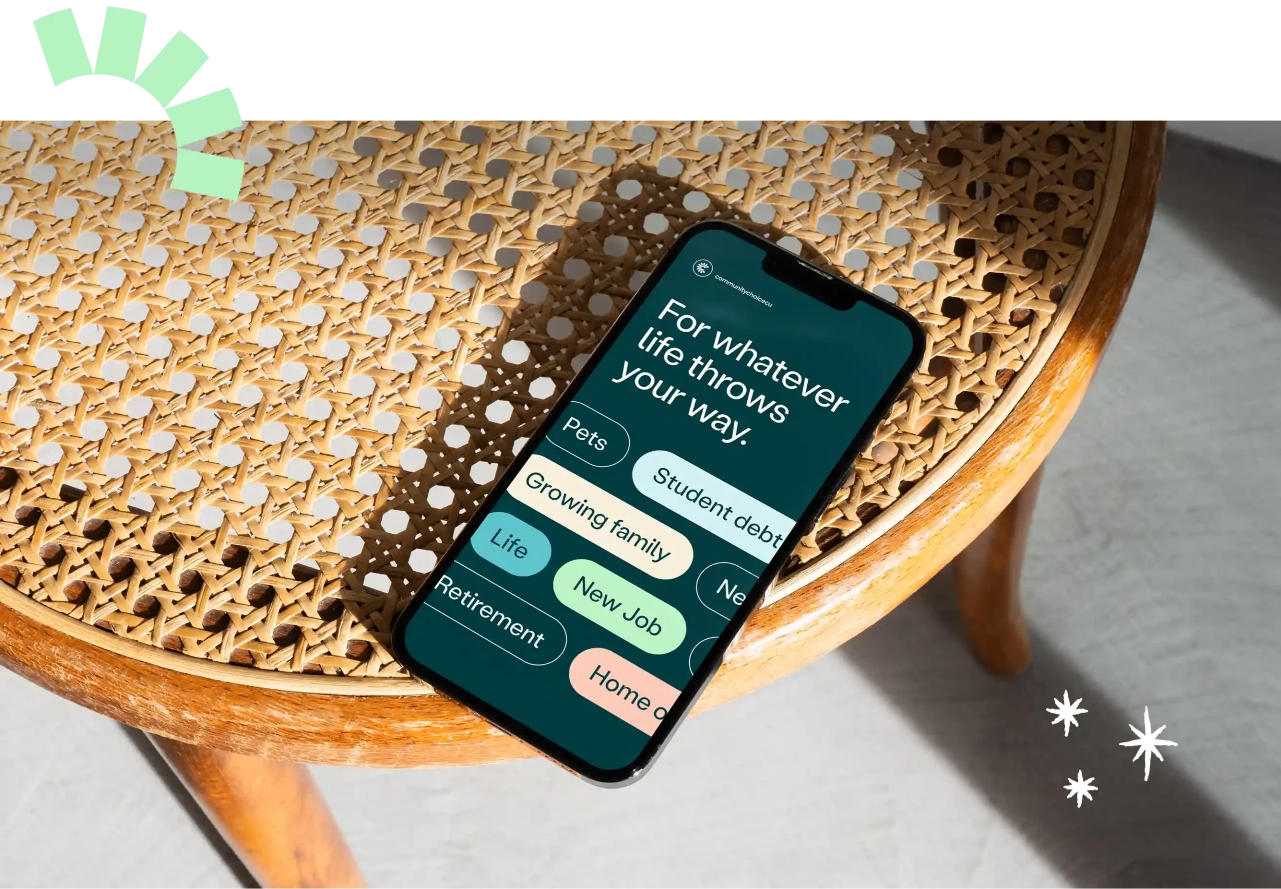 A smartphone on a woven chair displays an app with categories like Growing family, New Job, Pets, Student debt, and Retirement. Decorative star and arch shapes are nearby.