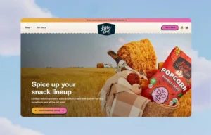 A basket with popcorn, pumpkins, and a blanket sits in a wheat field with hay bales. Text reads “Spice up your snack lineup” and promotes pumpkin spice popcorn.