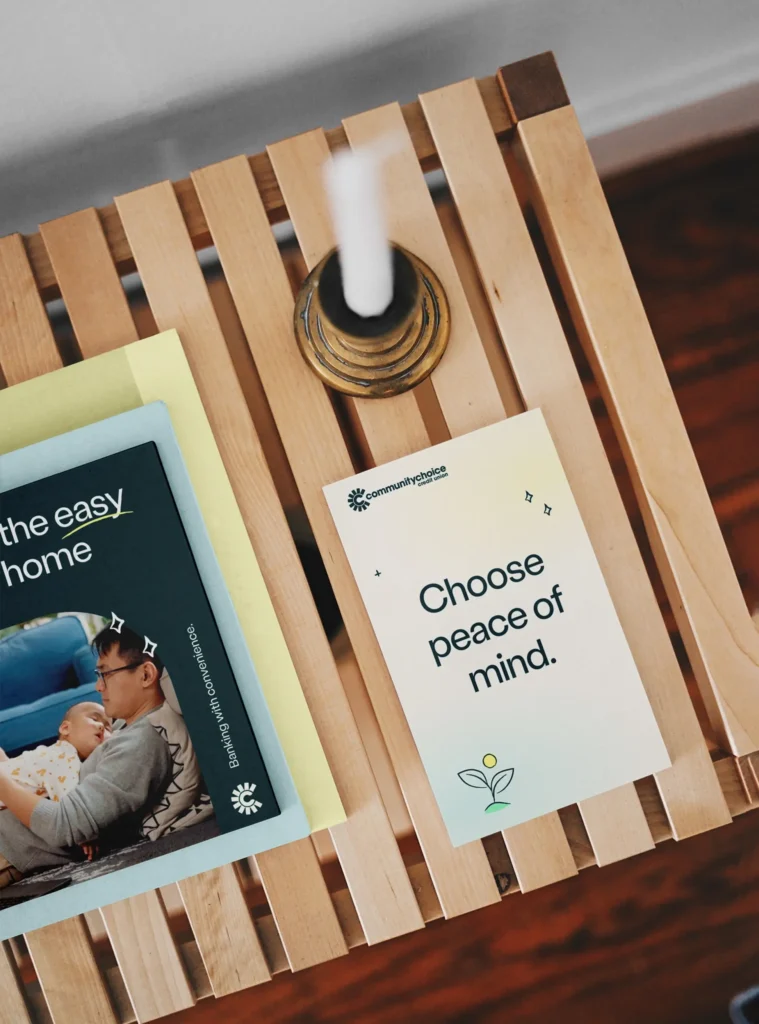 A wooden table holds a candle, a booklet with a photo of a man and child, and a card that reads Choose peace of mind.