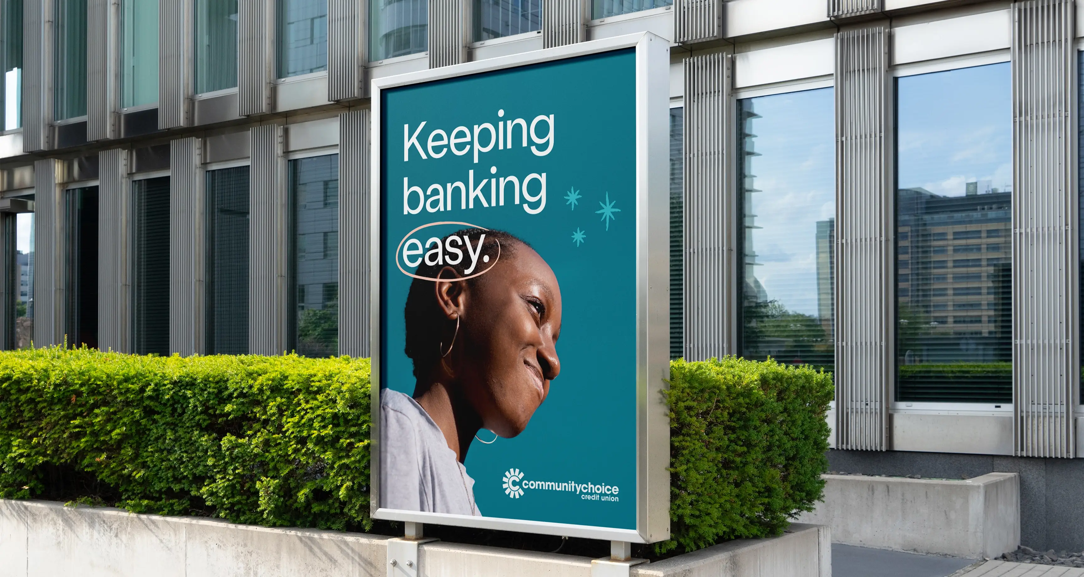 A billboard outside a modern building displays a smiling woman and the text, Keeping banking easy, with the Community Choice Credit Union logo at the bottom.