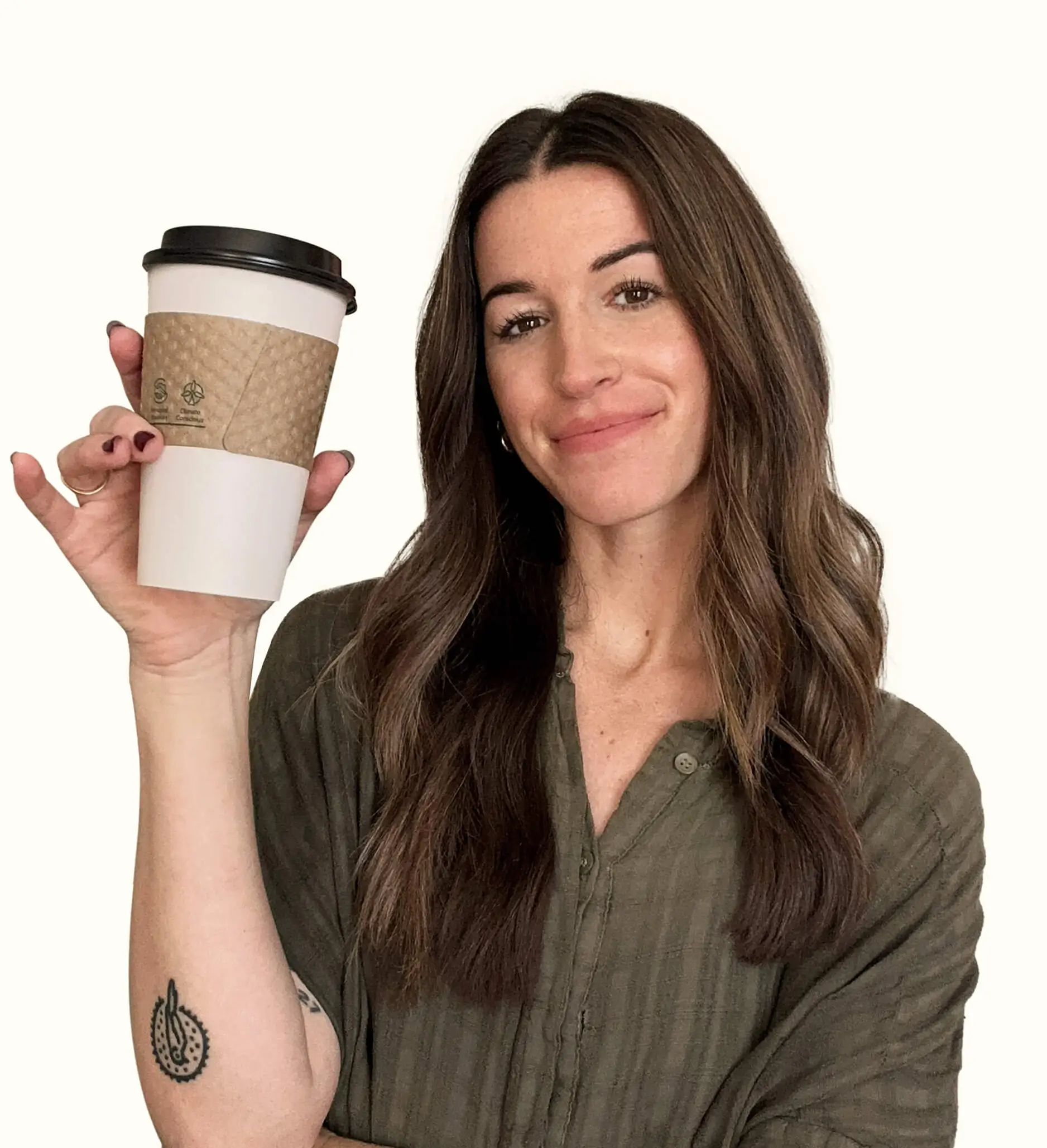 Woman with long brown hair, wearing a green shirt, smiling and holding up a takeaway coffee cup. She has a small tattoo on her forearm.