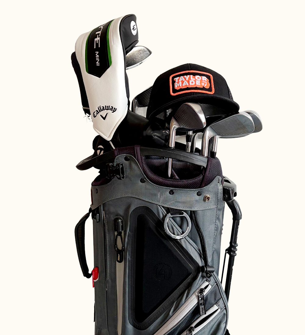 A gray golf bag filled with golf clubs, a Callaway club headcover, and a black TaylorMade cap resting on top.